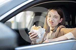 Happy woman eating a burger in the car