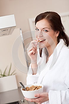 Happy woman eating cereals in kitchen