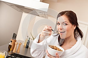 Happy woman eating cereals in kitchen