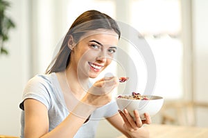 Happy woman eating cereals looking at you in a house