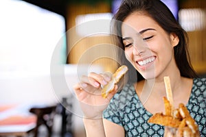 Happy woman eating chicken fingers alone in a restaurant