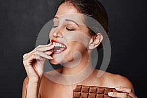 Happy, woman and eating with chocolate in studio for temptation of unhealthy snack. Female person, biting and dessert