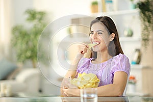 Happy woman eating potato chips at home