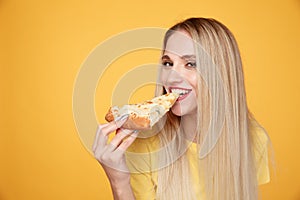 Happy woman eating tasty pizza for lunch in the yellow studio.