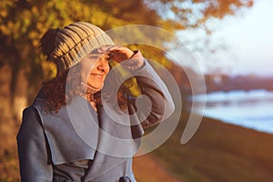 Happy woman enjoying beautiful autumn view. Autumn fashion, lifestyle concept. Woman wearing trendy coat and knitted headdress.