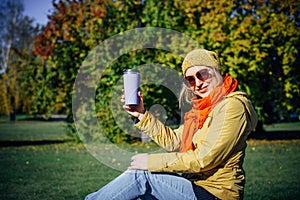 Happy woman enjoying coffee on park bench on green foliage background. Autumn concept. Leisure time in sunny fall day. Copy space