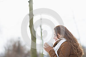 Happy woman enjoying cup of hot beverage in winter outdoors