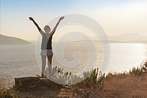 Happy woman enjoying freedom with open hands on the rock on sea background.