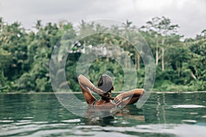 Woman enjoying tropical rain while swimming in infinity pool on Bali photo