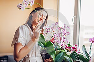 Happy woman enjoys blooming white orchid holding pot. Girl gardener taking care of home plants and flowers.