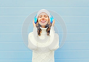 Happy woman enjoys listens to music in headphones wearing a knitted hat, sweater