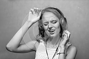 Happy woman enjoys music, wears stereo headphones, sings, closes her eyes
