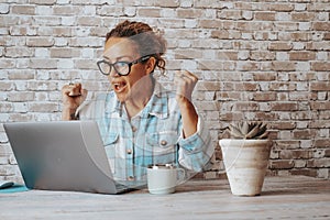 Happy woman exult and celebrate in front of a laptop after receiving a notification or email message. Overjoyed people working on photo