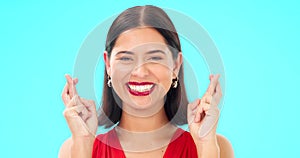 Happy, woman and face with fingers crossed on blue background, studio and wishing for good luck. Portrait of excited