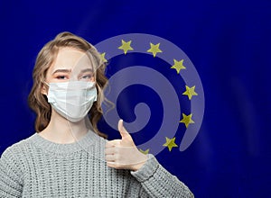 Happy woman in face mask holding thumb up on EU flag background. Flu epidemic and virus protection concept