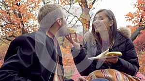A happy woman is feeding a bearded man a sandwich with cheese in the middle of an autumn park, slow motion
