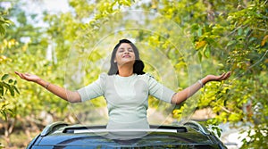 Happy woman feeling nature fresh air by stretching arms on car sunroof - concept of freedom, traveller and refreshment