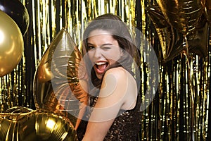 Happy woman in festive outfit holding gold balloons