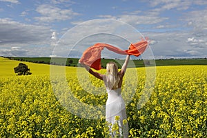 Happy woman flailing scarf in a field of flowering canola in spring