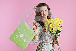 happy woman in floral dress with yellow chrysanthemums flowers and green shopping bag isolated on pink background