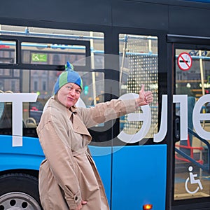 A happy woman in a funny hat near a blue electric bus