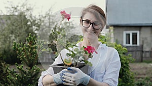 Happy woman gardener holding flowers smiling at camera while working in her garden in spring