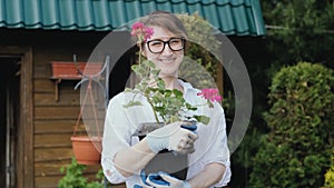 Happy woman gardener holding flowers smiling at camera while working in her garden in spring
