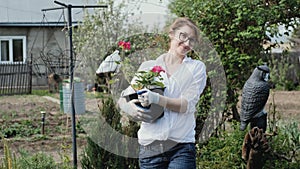 Happy woman gardener holding flowers smiling at camera while working in her garden in spring