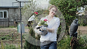 Happy woman gardener holding flowers smiling at camera while working in her garden in spring