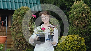 Happy woman gardener holding flowers smiling at camera while working in her garden in spring