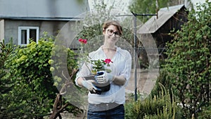 Happy woman gardener holding flowers smiling at camera while working in her garden in spring