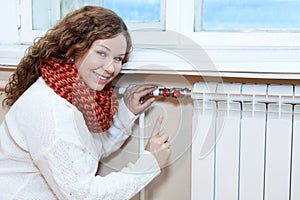 Happy woman gesturing when controling thermostat on central heating radiator