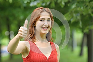 Happy woman gesturing thumbs up at camera in a park