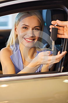 Happy woman getting car key in auto show or salon