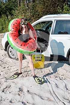 happy woman getting out from the car in flippers with inflatable ring and bag