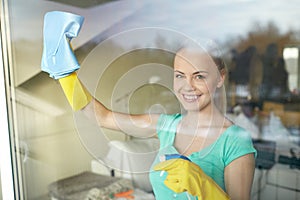 Happy woman in gloves cleaning window with rag