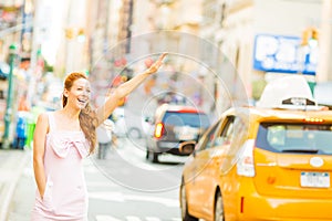 A happy woman hailing a yellow taxi while walking on a street in New York city