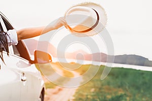 Happy woman hand holding hat outside open window car with meadow and mountain lake background. People lifestyle relaxing as