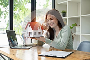 Happy woman hand holding magnifying glass and looking at house model, house selection, real estate concept.