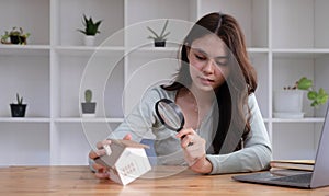 Happy woman hand holding magnifying glass and looking at house model, house selection, real estate concept.