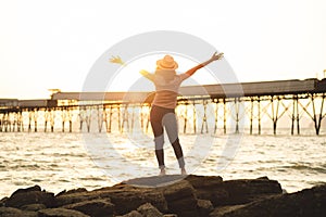 Happy woman with hands up standing on sunset beach in summer wit