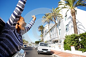 Happy woman hanging outside car window with arms raised