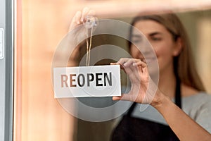 happy woman hanging reopen banner on door glass