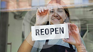 happy woman hanging reopen banner to door glass