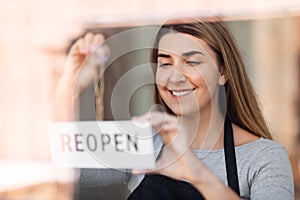 happy woman hanging reopen banner to door glass