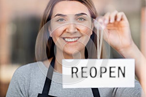 happy woman hanging reopen banner to door glass