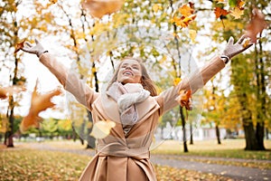 Happy woman having fun with leaves in autumn park