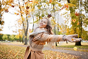 Happy woman having fun with leaves in autumn park