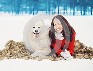 Happy woman having fun with white Samoyed dog outdoors on the snow in winter day