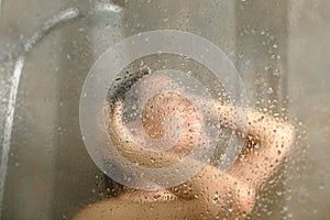 Happy woman having shower behind glass on a bathroom